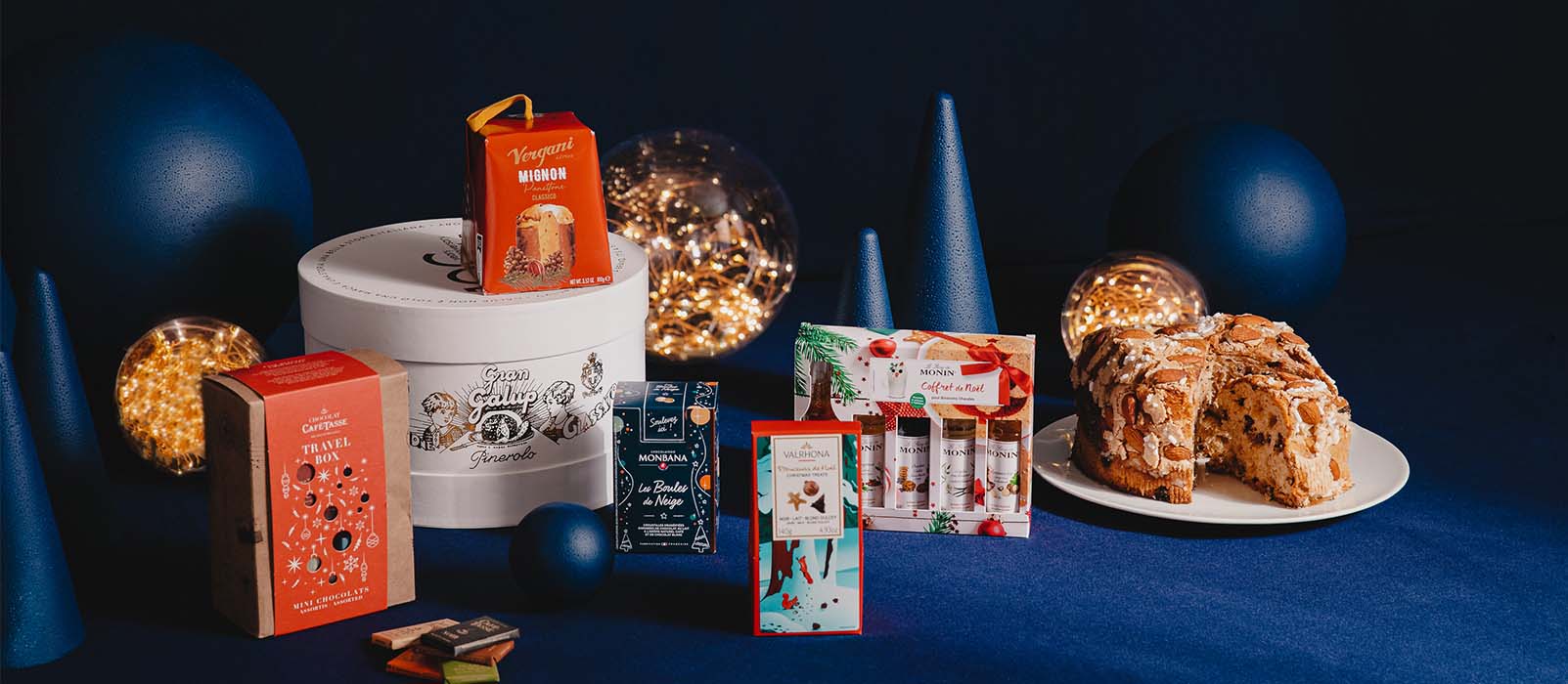 Produits gourmands et panettone sur table avec décorations festives bleues et lumières.